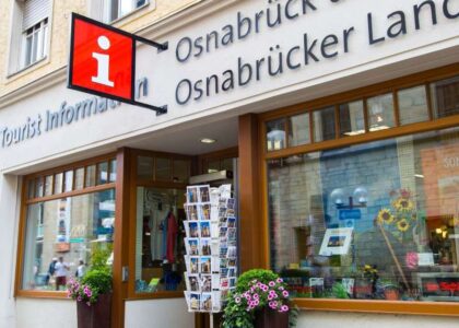Eingang der Tourist Information mit Postkartenständer, roten Info-Schildern und der Fassadenaufschrift: Osnabrück und Osnabrücker Land.