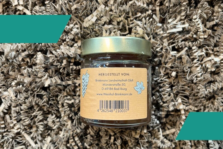 Kleines Geleeglas von hinten mit Adressangaben des Herstellers auf braunem Verpackungsmaterial.
