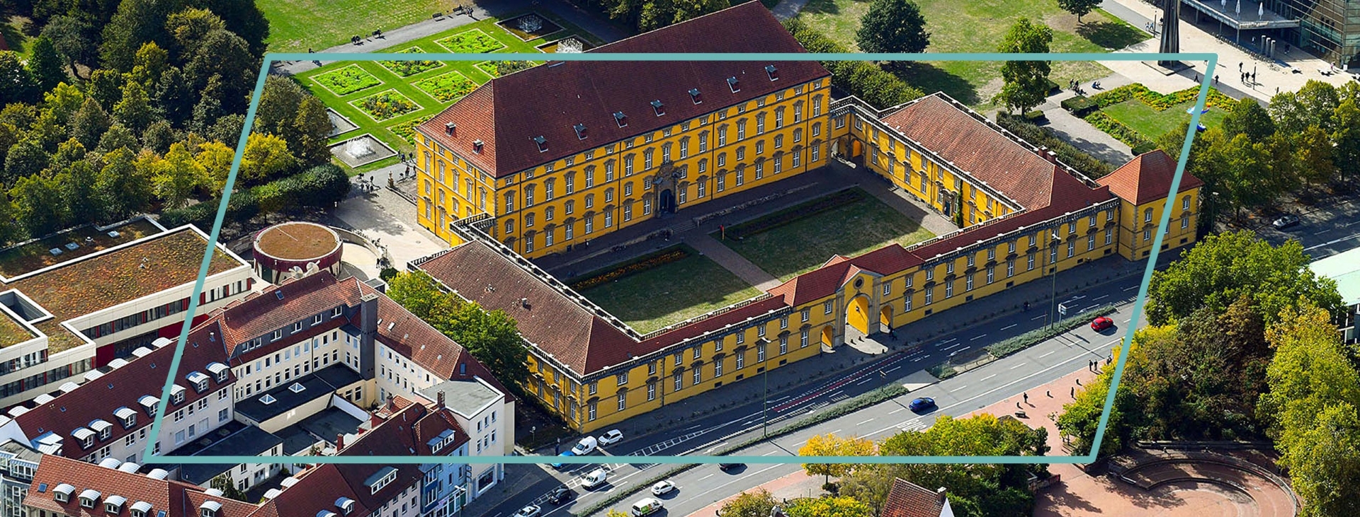 Luftaufnahme des gelben Osnabrücker Barockschlosses mit Innenhof, umgeben von Parkanlagen, modernen Universitätsgebäuden und Straßen.