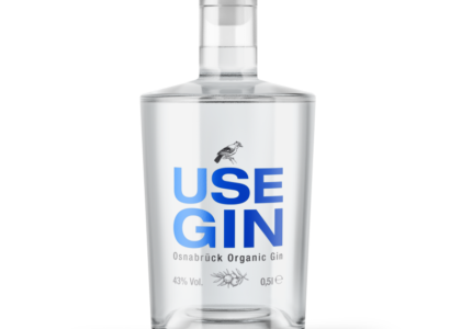 Durchsichtige Gin-Flasche mit Holzverschluss und blauem Schriftzug: Use Gin Osnabrück Organic Gin, sowie kleiner Vogel-Illustration.